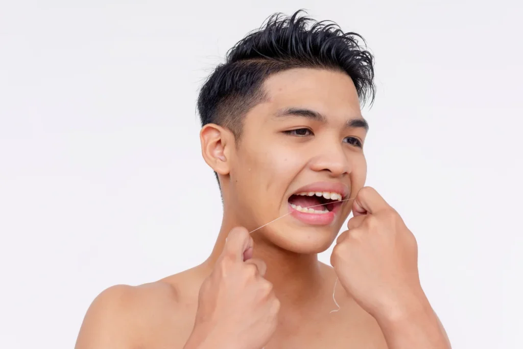 Young Asian man flossing his teeth after a tooth filling to maintain his restored tooth’s health
