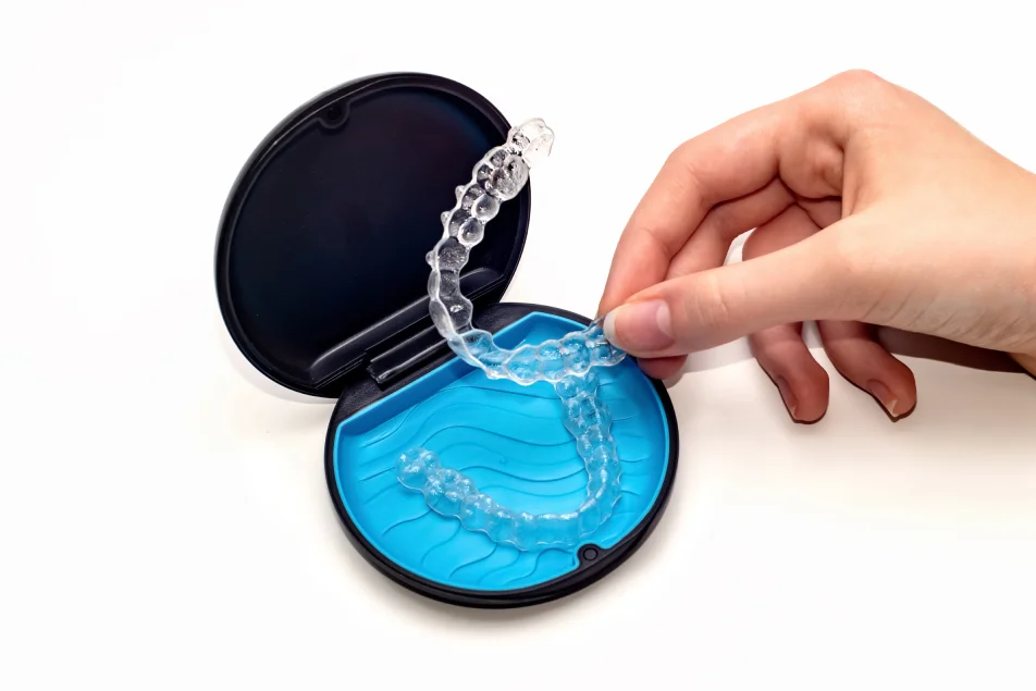  A Hand Holding Sets of Invisalign Aligners from a Storage Box 